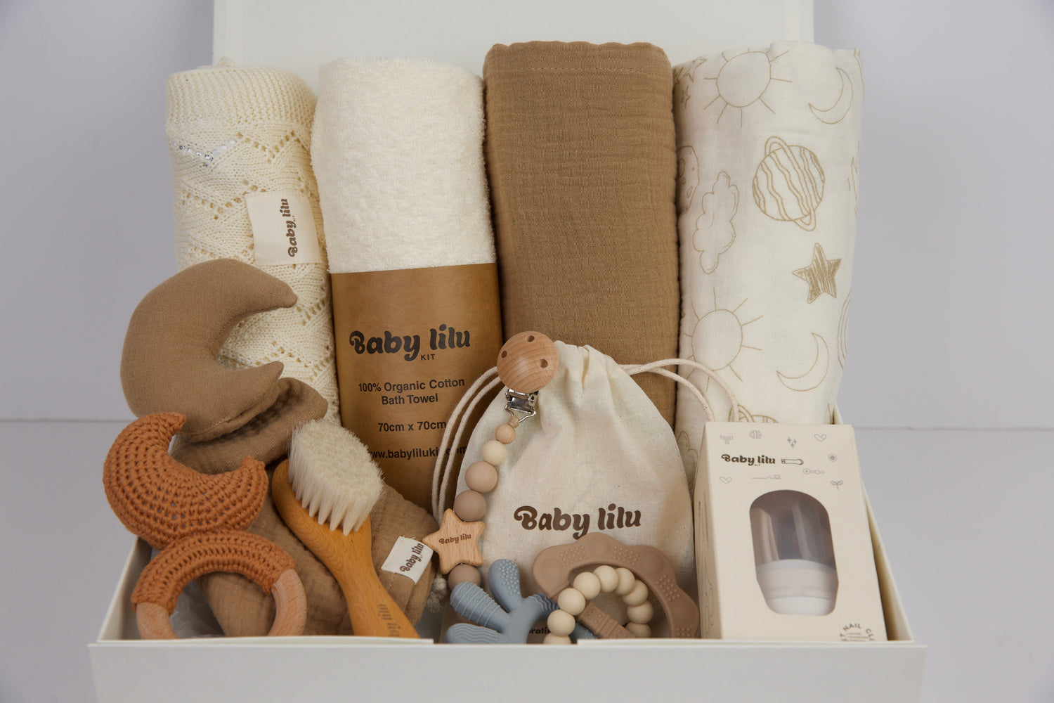 Over the Rainbow baby gift box with towel, blanket, teether, pacifier holder, rattle, nail care set, and milestone items in soft brown tones.