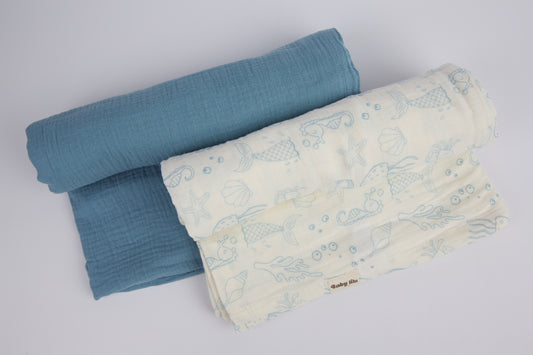 A set of two soft muslin swaddle blankets with an ocean theme in soothing blue shades. Perfect for swaddling, nursing, cuddling, or use as a play mat. 